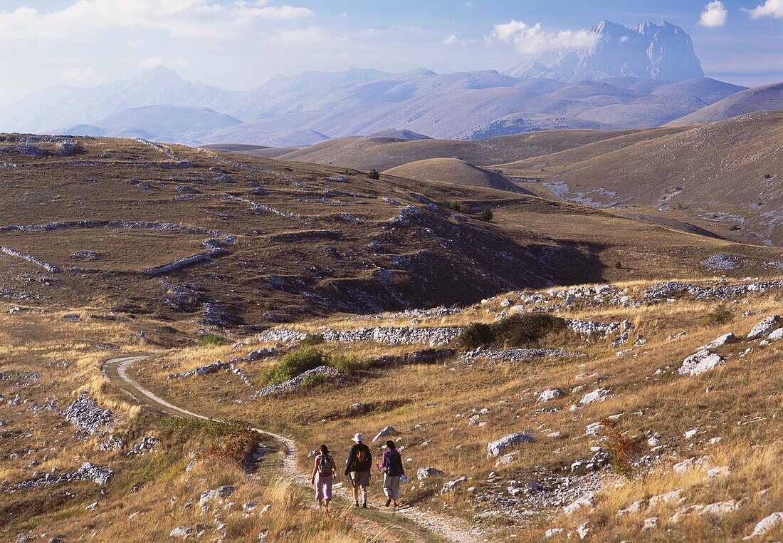 Frauen, die in der Nähe von Rocca Calascio mit dem Gipfel des Corno Grande im Hintergrund einen Weg entlanggehen