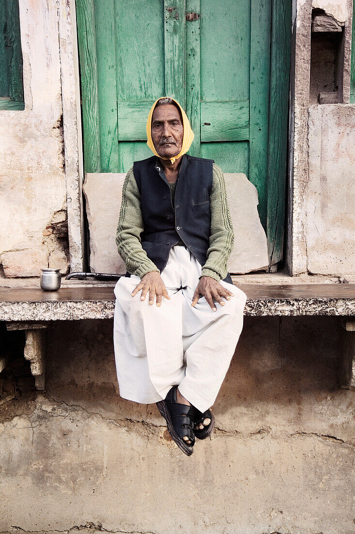 Älterer Mann sitzt vor einem Dorfgebäude