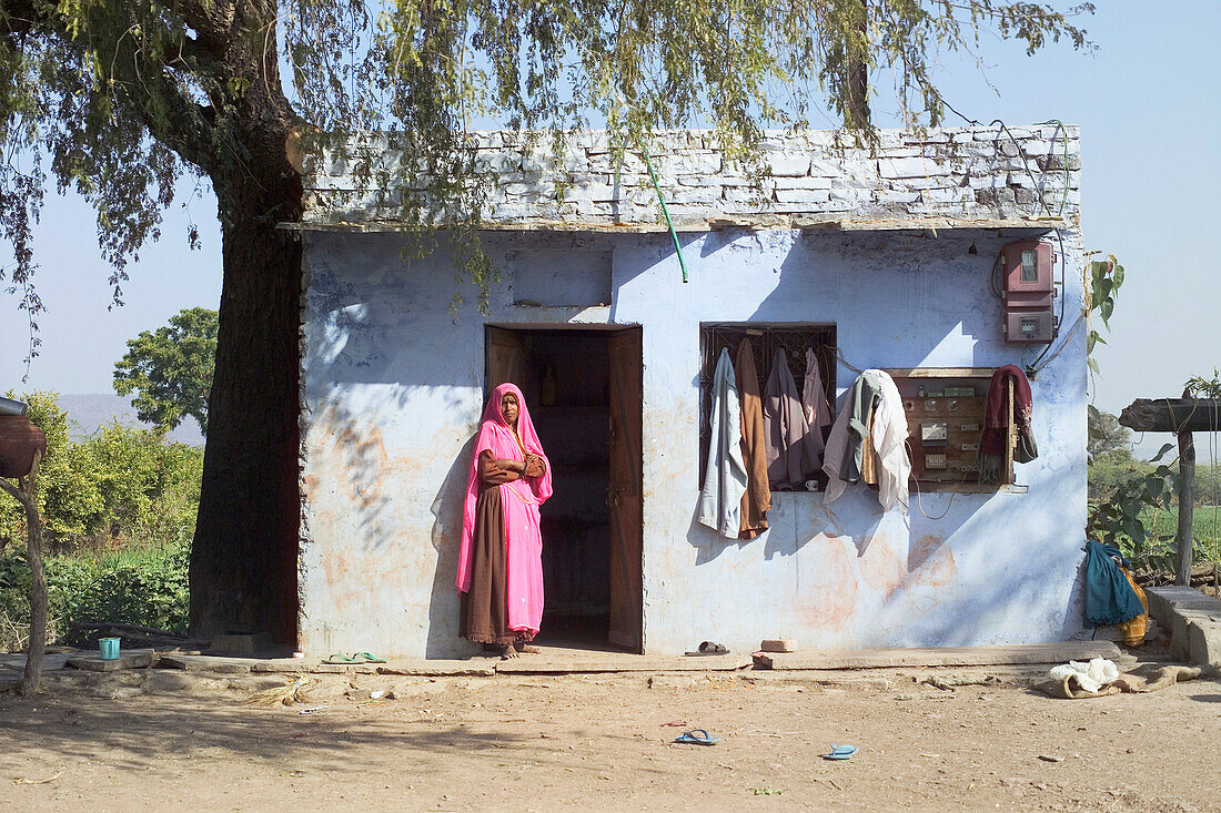 Frau in rosafarbenem Sari in der Tür ihres Dorfhauses stehend