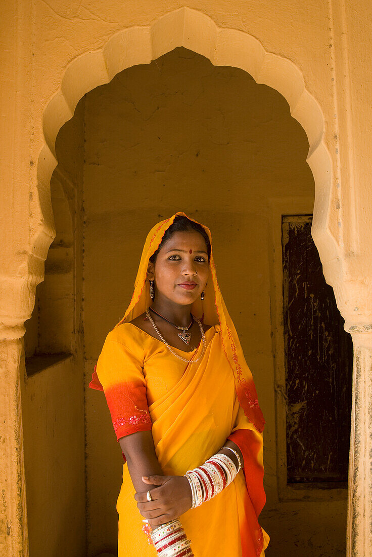 Frau in gelbem Sari im Torbogen eines alten Gebäudes