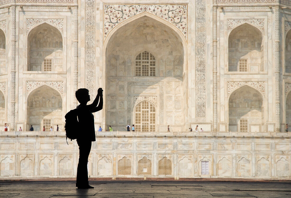 Silhouette einer Frau mit Rucksack beim Fotografieren des Taj Mahal