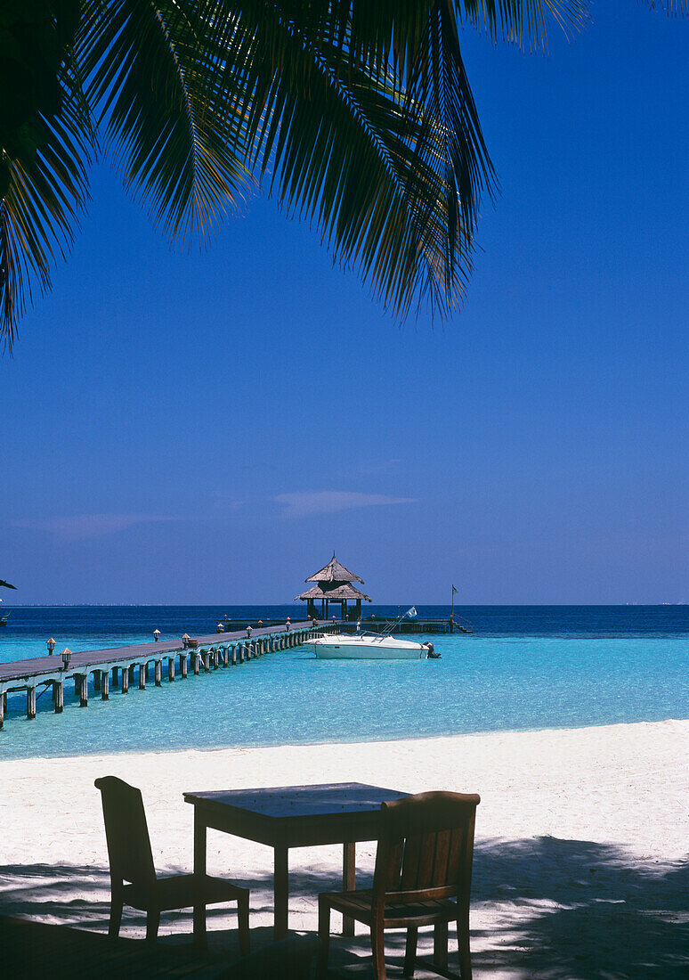 View Of Pier With Table And Chairs On White Sand Beach