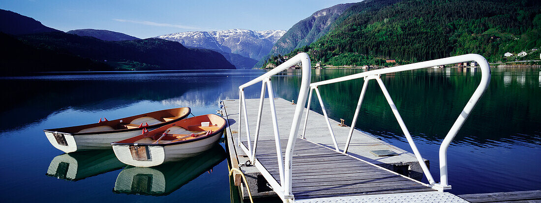 Row Boats By Jetty On Lake By Mountains