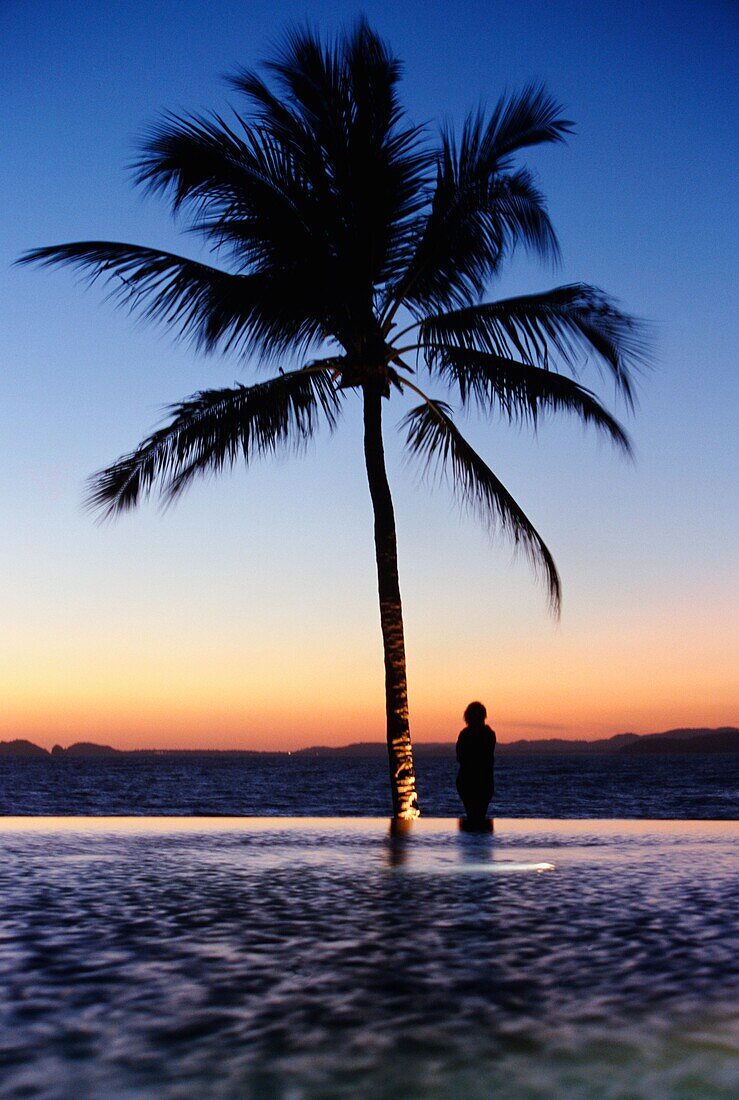 Frau stehend in Silhouette neben Infinity Pool an der Küste