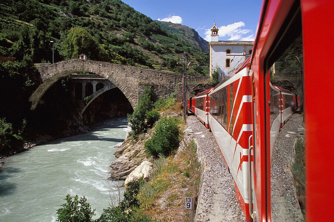 Roter Zug in der Kurve bei Bach und Brücke