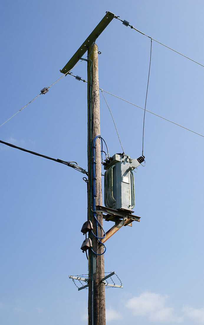 Telephone and electricity cables and post against a blue sky; England