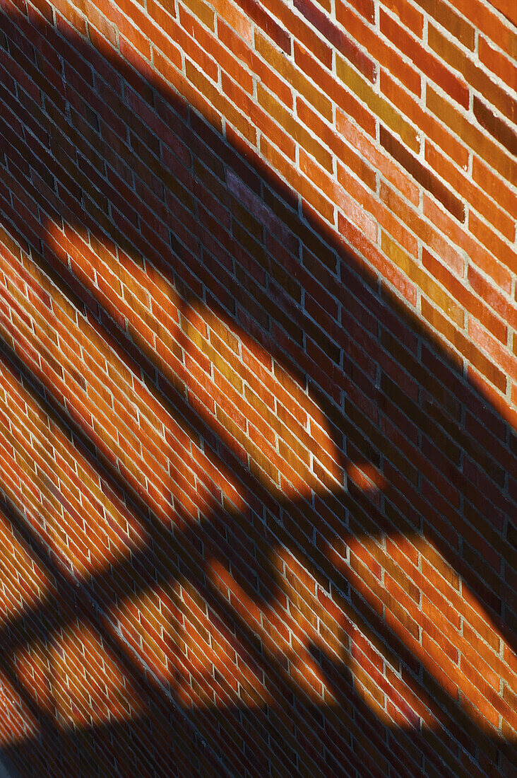 Eine braune Backsteinmauer mit dem Schatten eines Geländers; Hamburg, Deutschland