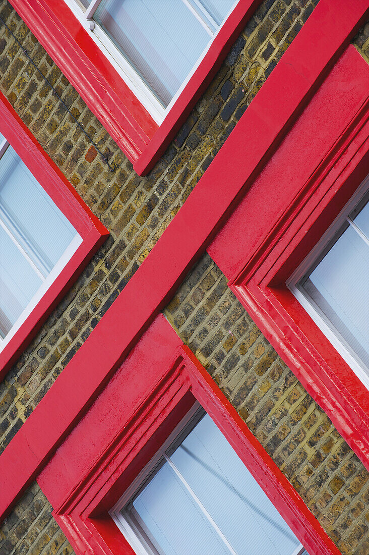 Leuchtend rote Umrandung von Fenstern an einem Backsteingebäude; London, England