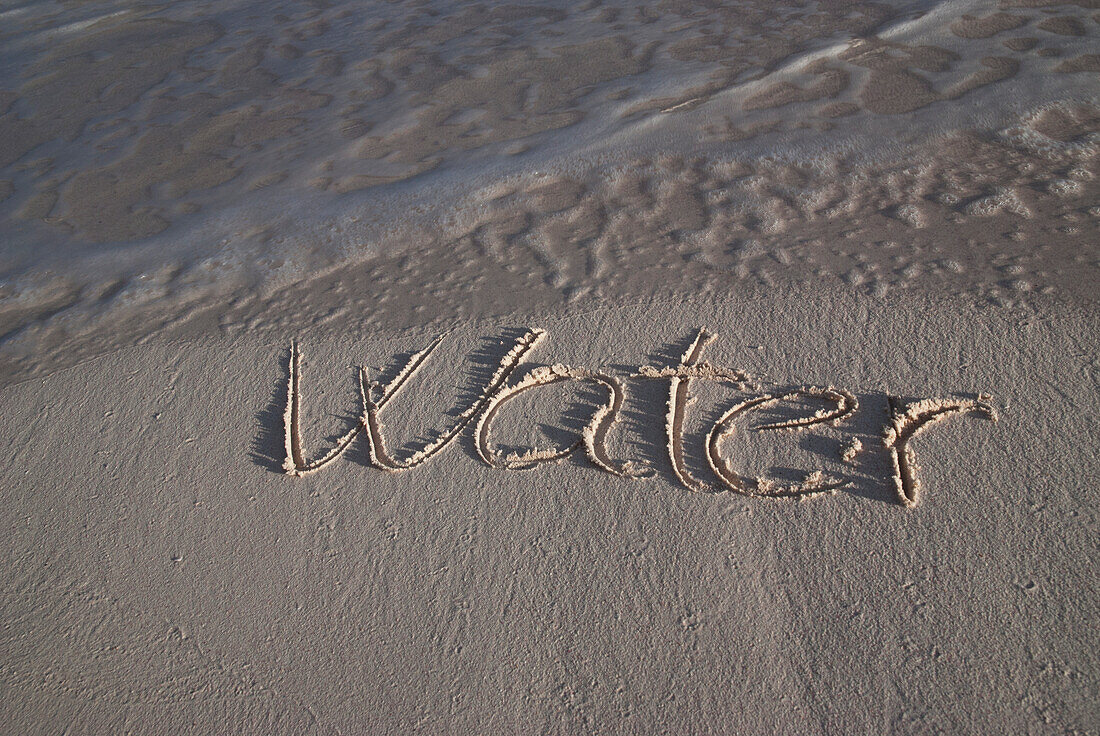 Das Wort Wasser handgeschrieben im Sand am Wasser; Tulum, Mexiko