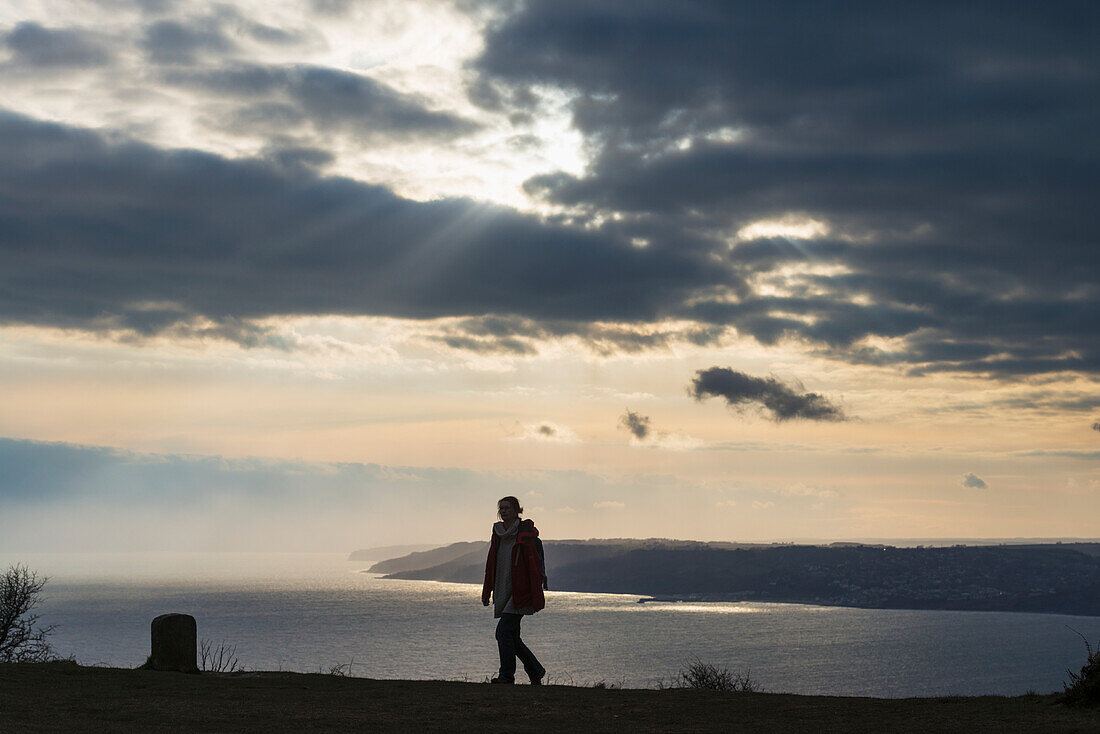 Woman Walking Near The Top Of Golden Cap With Lyme Regis Behind, Jurassic Coast; Dorset, England