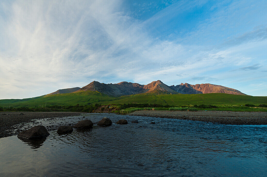 Looking Across A Small River To The Peaks And Ridges Of The Black Cuillin At Sunset; Isle Of Skye, Scotland