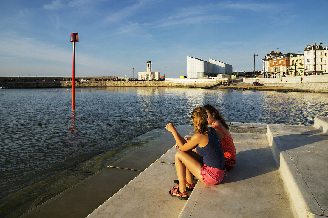 Teenage Girls Sitting On Steps Along The Waterfront; Margate, Kent, England