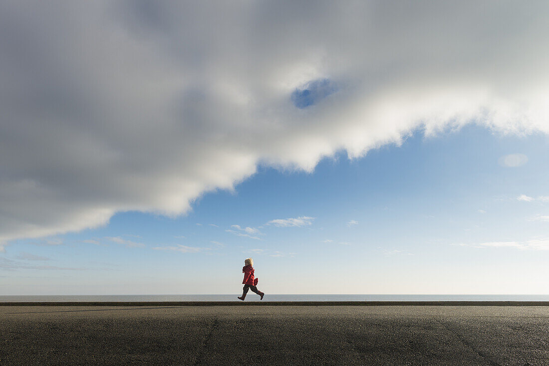 Boy Running Along Sea Wall; Aldeburgh, Suffolk, England