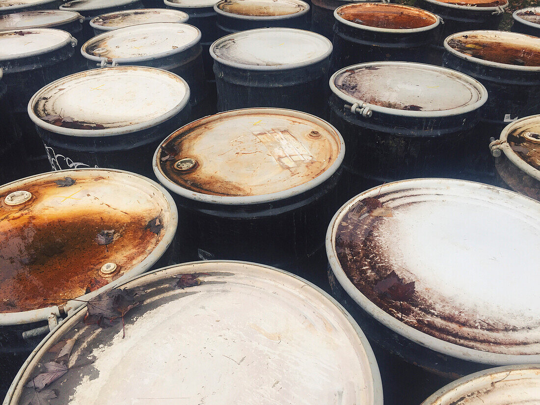 Rusty oil barrels packed closely together, wet and damaged.