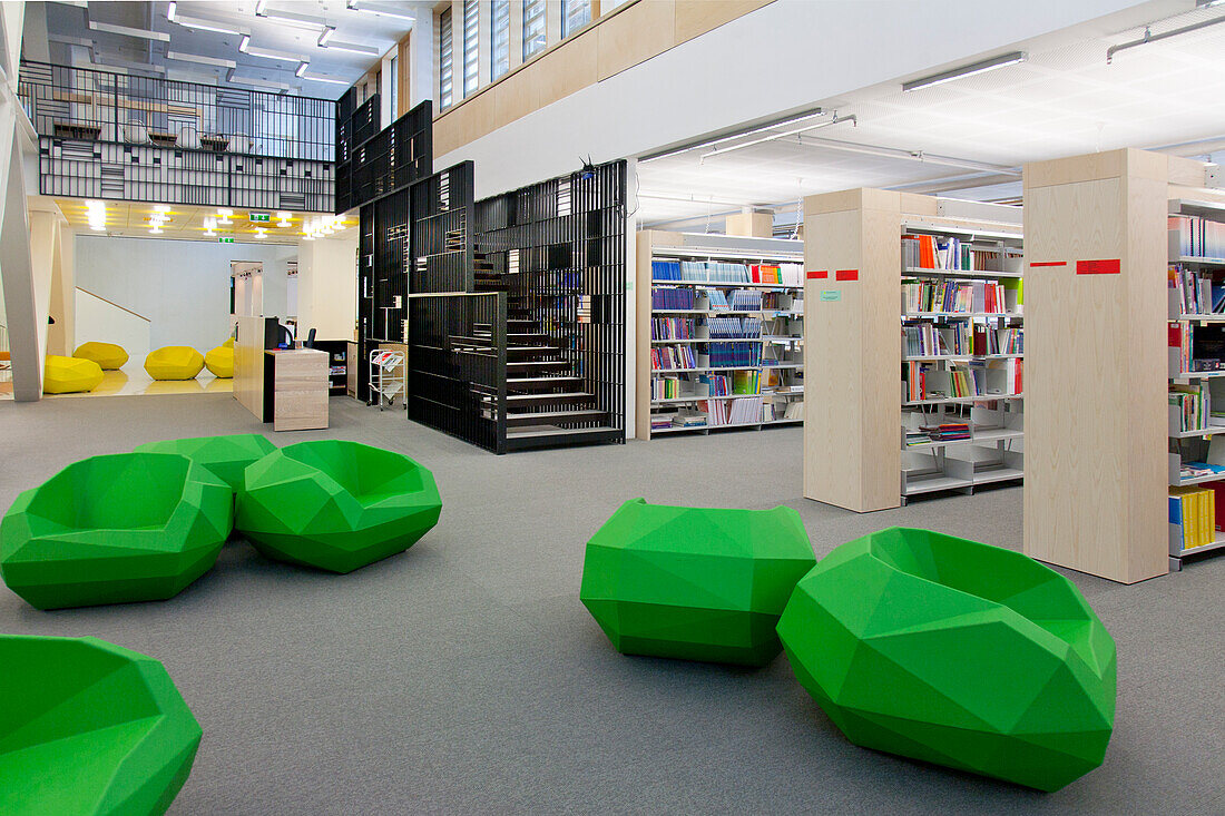 Eine Hochschulbibliothek im Gesundheitswesen mit offenen Räumen, grünen Stühlen und Bücherstapeln. Ein modernes, helles und luftiges Gebäude. 
