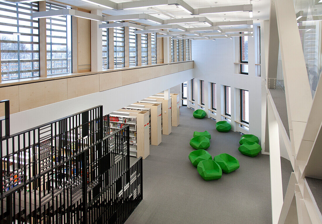 A healthcare college library with open spaces, green chairs and book stacks. A modern light and airy building. 