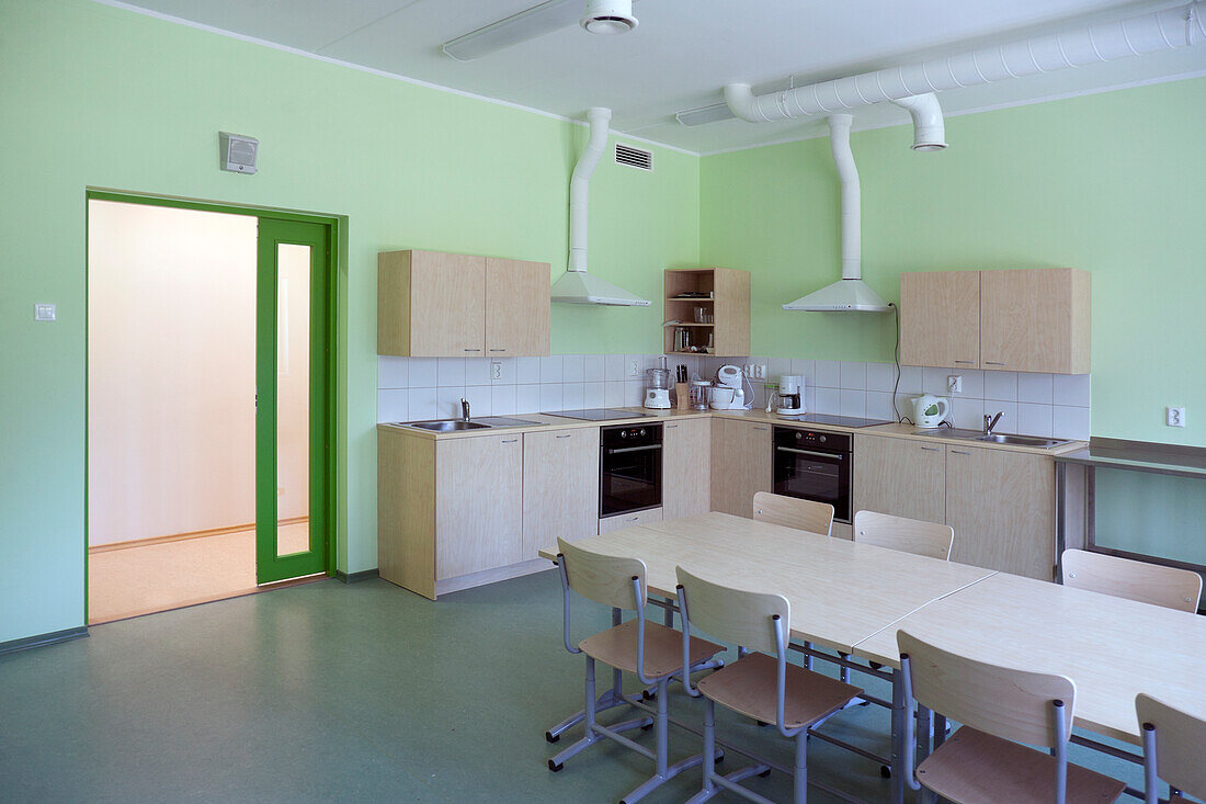 A modern school, a kitchen with fitted cupboards and ovens, a long table and chairs.