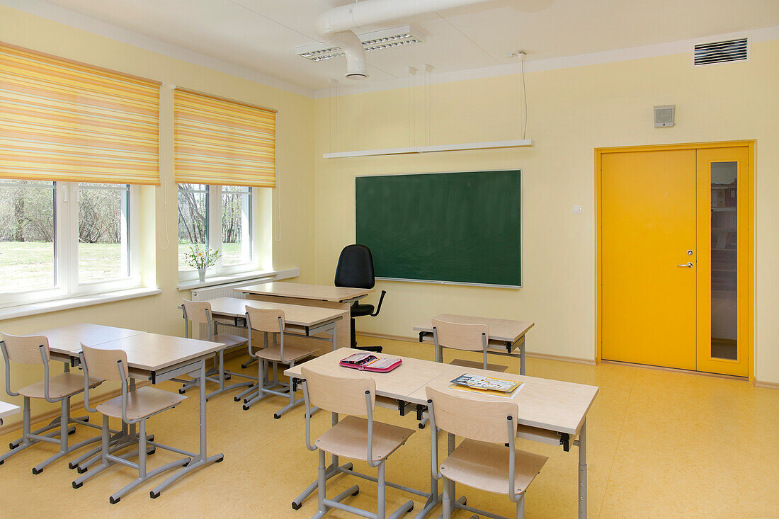 A newly built school classroom with desk and chairs. Windows with yellow blinds. 