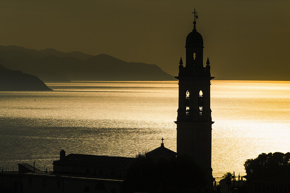 Goldenes Sonnenlicht reflektiert auf dem Wasser in der Abenddämmerung mit dem Turm der Kirche; San Lorenzo Della Costa, Ligurien, Italien