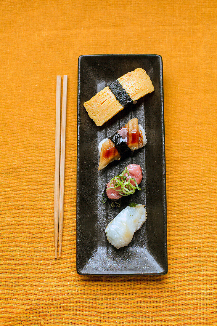 Sushi-Platte, eine Auswahl an rohem Fisch und Reissnacks mit Essstäbchen. 