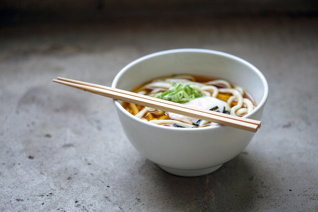 A bowl of noodles, vegetables and broth and a set of chopsticks. 