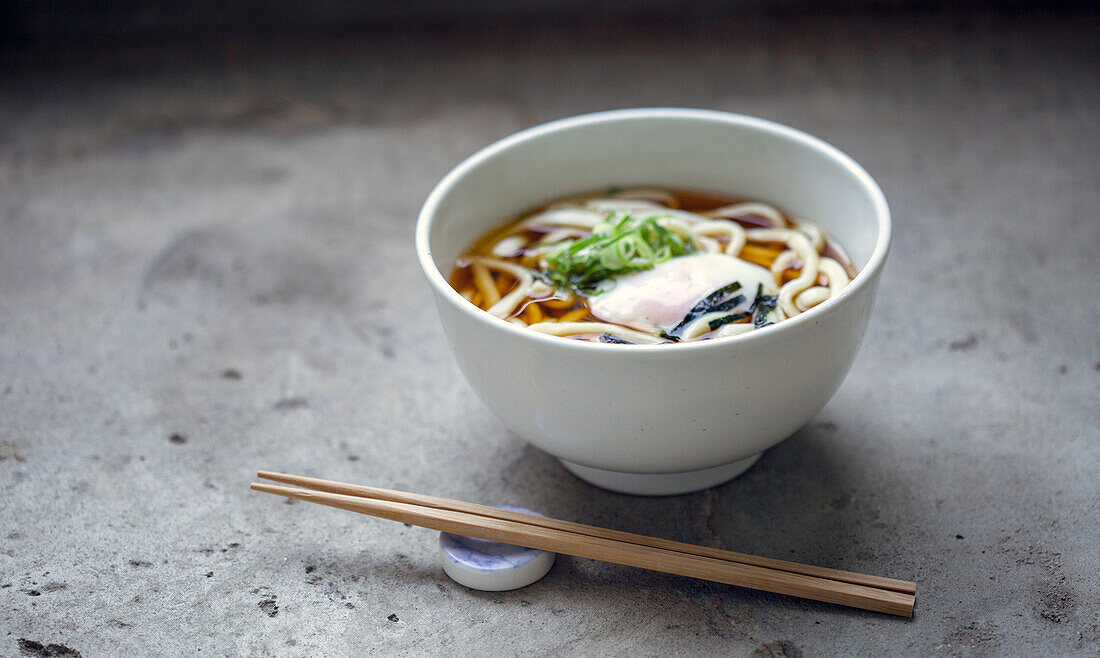 A bowl of noodles, vegetables and broth and a set of chopsticks. 