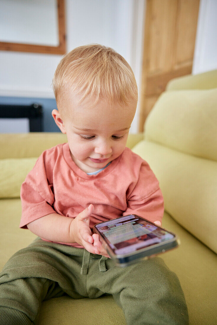 Kleinkind schaut drinnen auf sein Smartphone