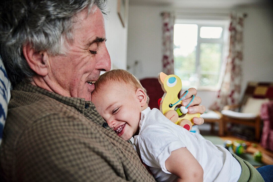 Nahaufnahme eines lachenden Kleinkindes in den Armen seines Großvaters