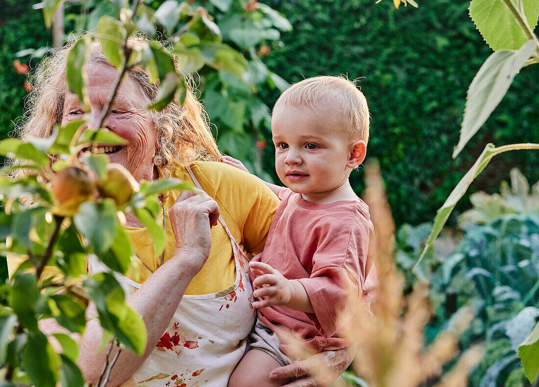 Großmutter hält Kleinkind auf der Hüfte im Garten