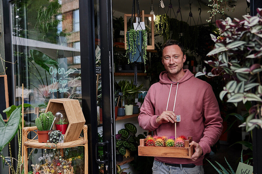 Portrait of man holding tray of cacti in doorway of flower shop