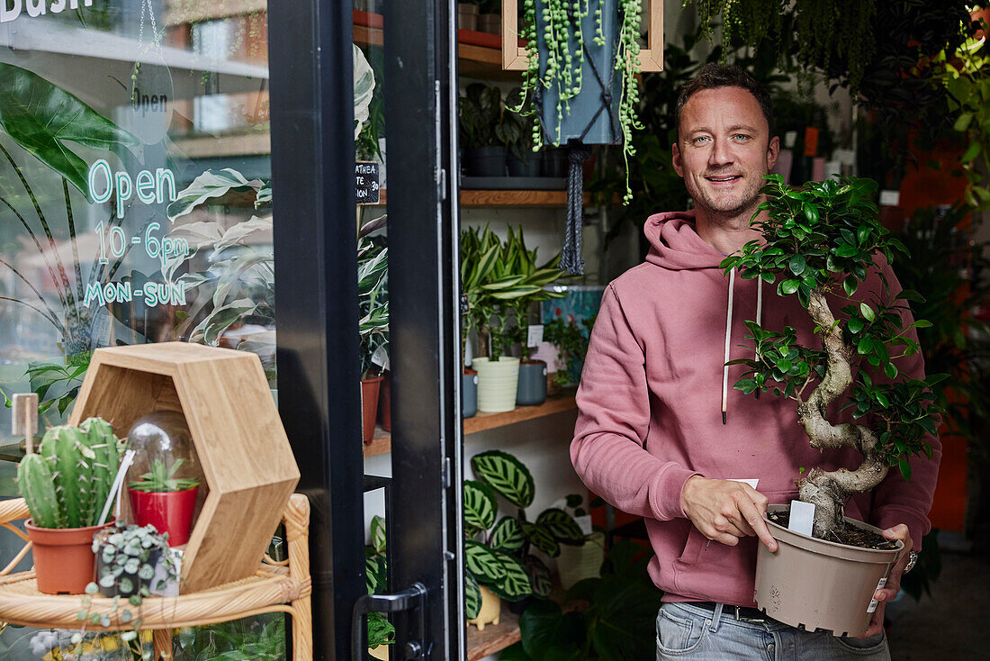 Porträt eines Mannes, der in der Tür eines Blumenladens steht und eine Pflanze hält