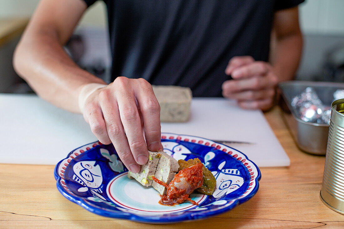 A man preparing food in a restaurant, placing vegetables and pate on a plate. Close up.