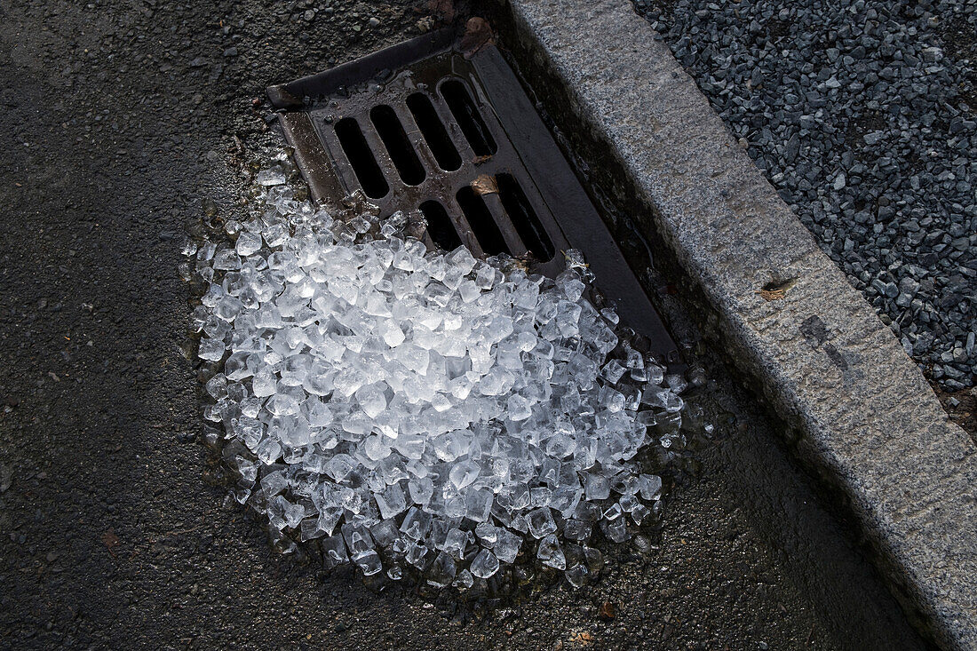 A pile of melting, discarded ice by a street drain on a street. 
