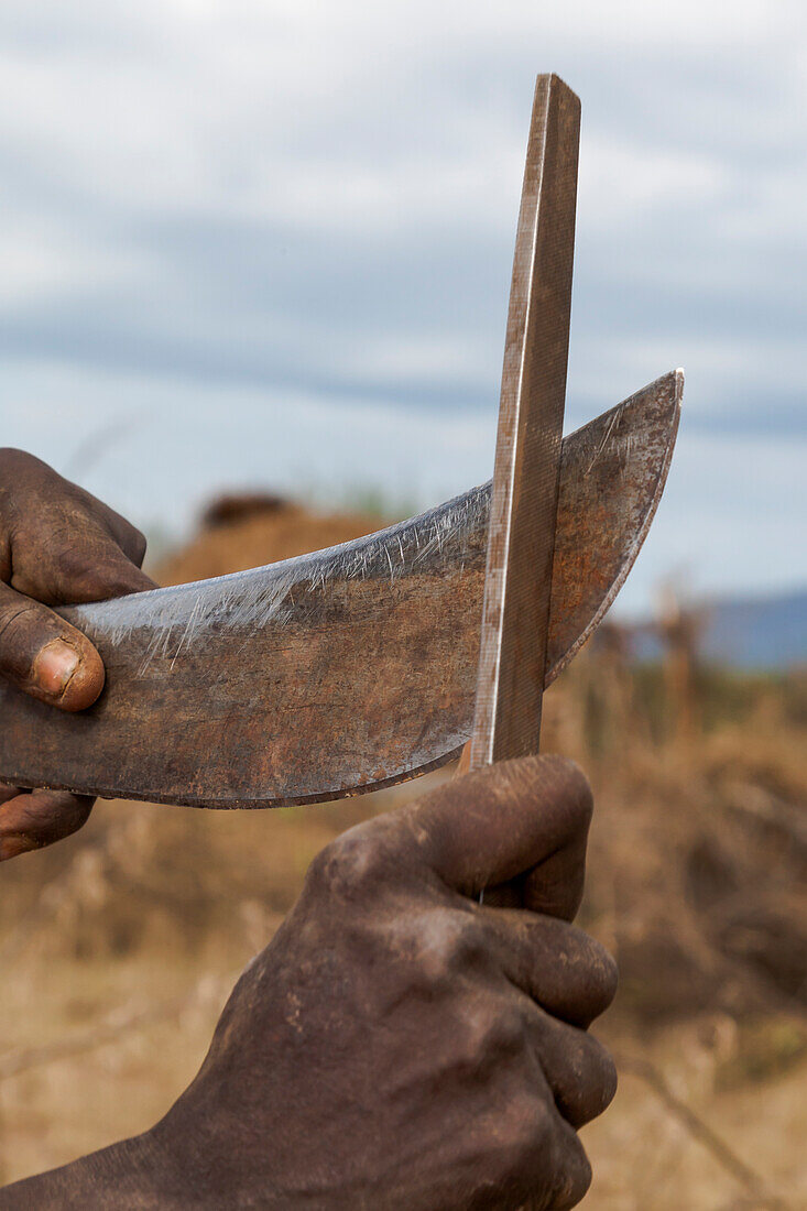 Africa, Ethiopia, Southern Omo Valley, Mursi Tribe. The panga of a Mursi man being sharpened with his file.
