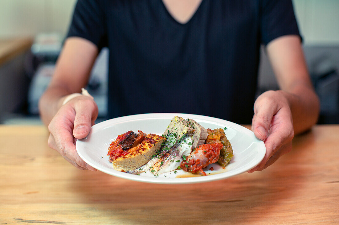 A man standing at a restaurant counter presenting plates of cooked food, menu dishes.