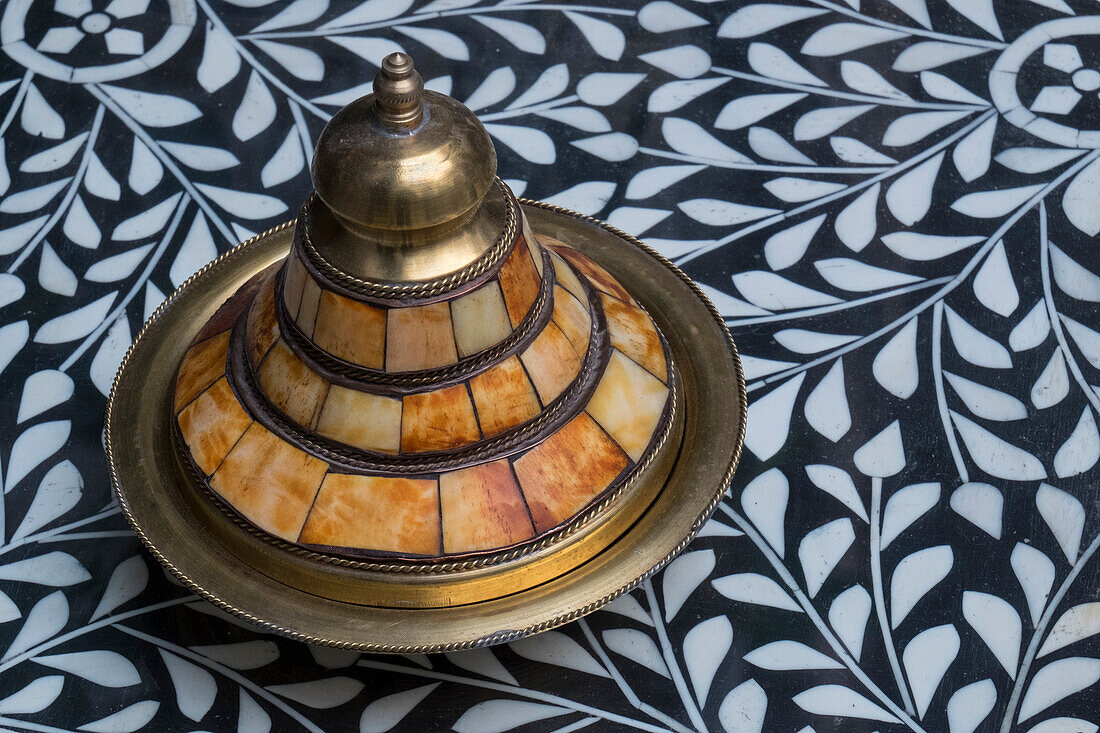 Marokko, Fes. Eine abgedeckte Messingschale mit Kamelknocheneinlage steht auf einem Tisch mit Steineinlegearbeiten in einem Geschäft.
