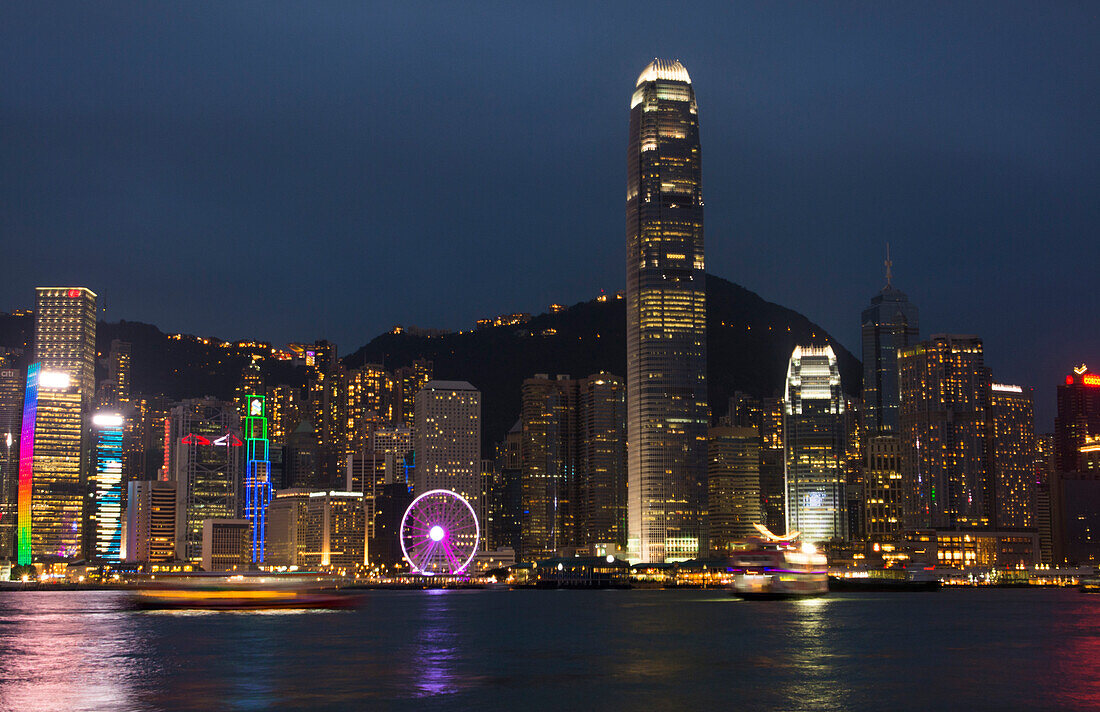 Hong Kong, China. Skyline harbor with new Ferris Wheel and reflections on water and mountain peak in background