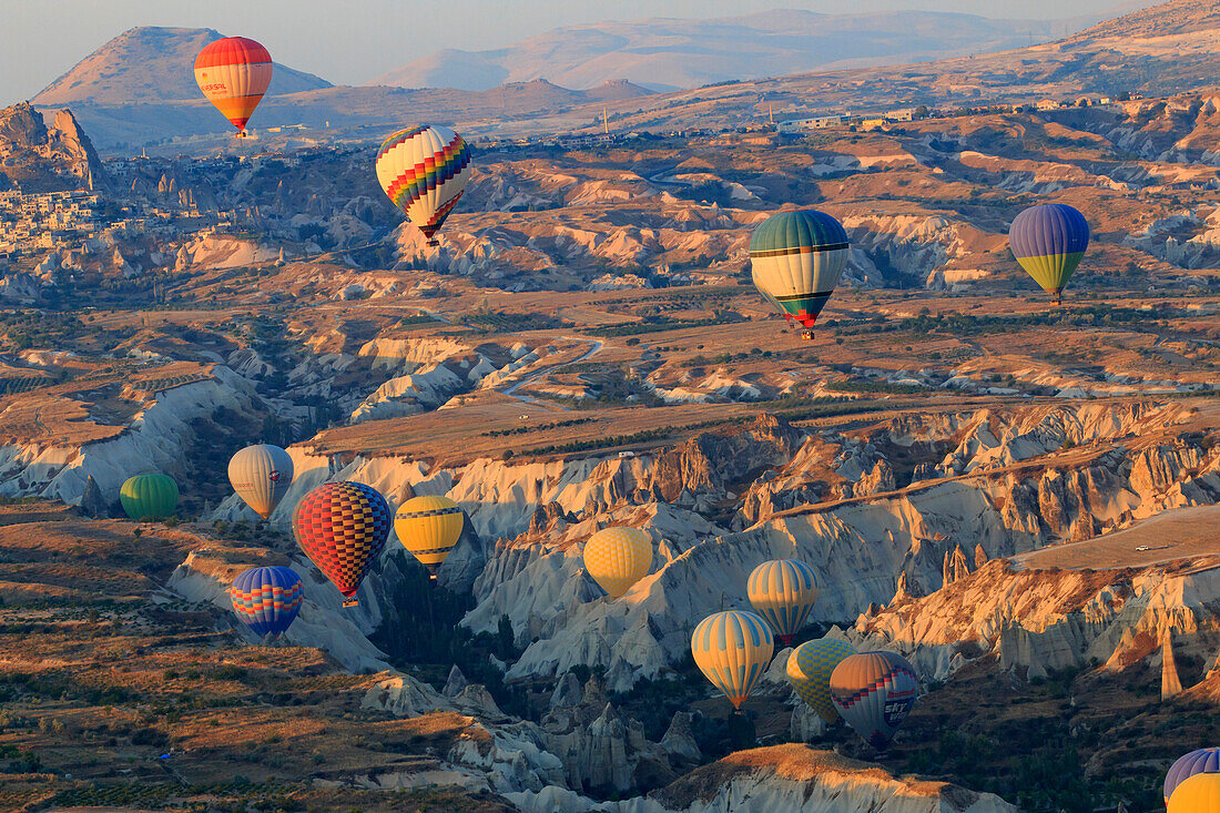 Turkey, Anatolia, Cappadocia, Goreme. Hot air balloons flying above rock formations and field landscapes in the Red Valley, Goreme National Park, UNESCO World Heritage Site.