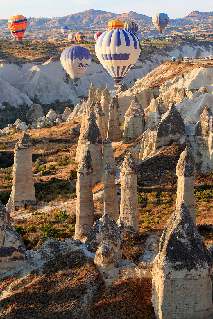 Turkey, Anatolia, Cappadocia, Goreme. Hot air balloons flying above rock formations, 'Fairy Chimneys' and field landscapes in the Red Valley, Goreme National Park, UNESCO World Heritage Site.