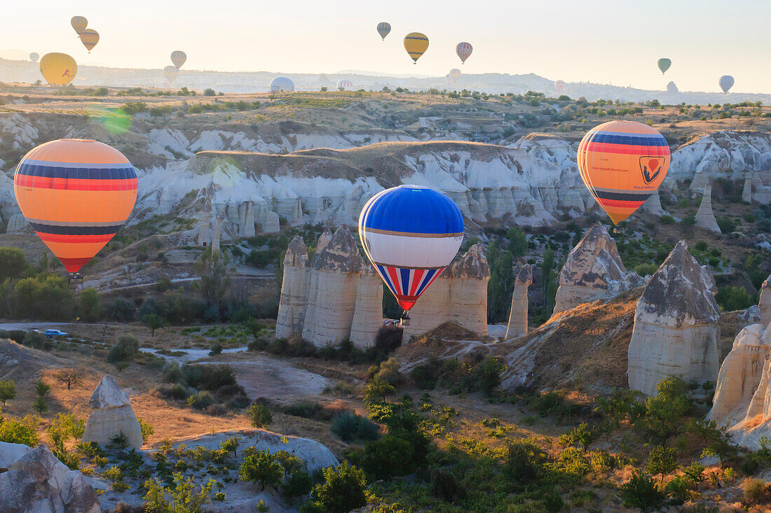Türkei, Anatolien, Kappadokien, Goreme. Heißluftballons fliegen über Felsformationen und Feldlandschaften im Goreme-Nationalpark, UNESCO-Welterbe.