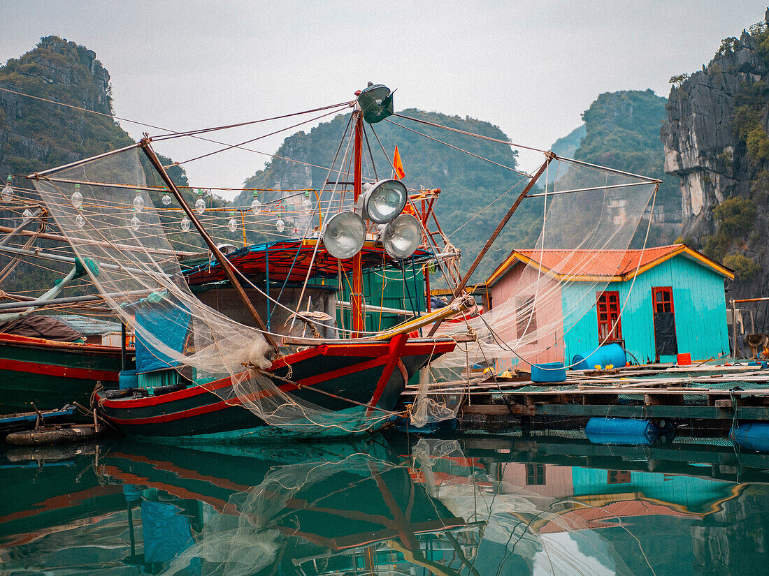 Asien, Vietnam, Quang Ninh, Ha Long Bucht. Ein farbenfrohes Fischerboot am Dock spiegelt sich im ruhigen Wasser der Bucht.