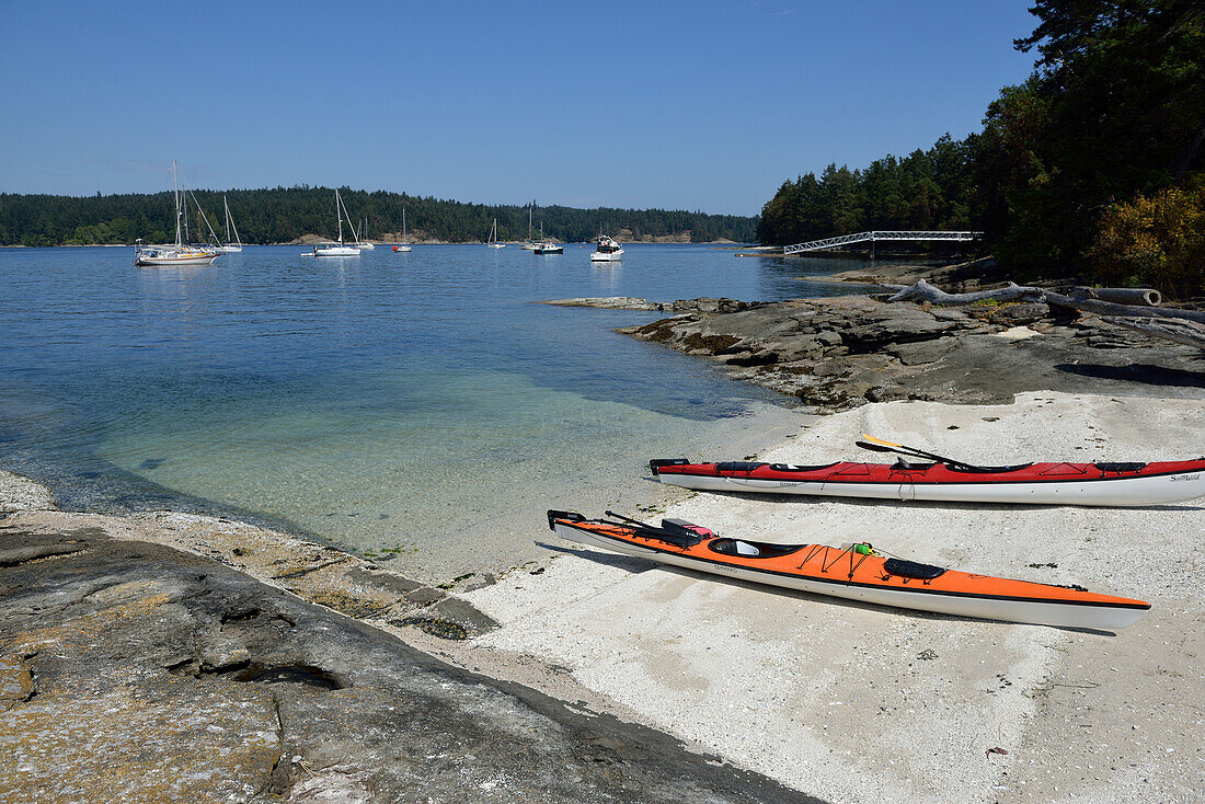 Canada, British Columbia, Russell Island. Kayaks on a shell beach in front of anchored boats.