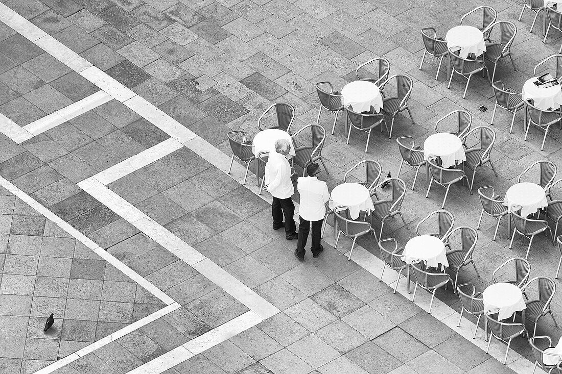 Italy, Venice. Black and white looking down on waiters in San Marco Square from Campanile