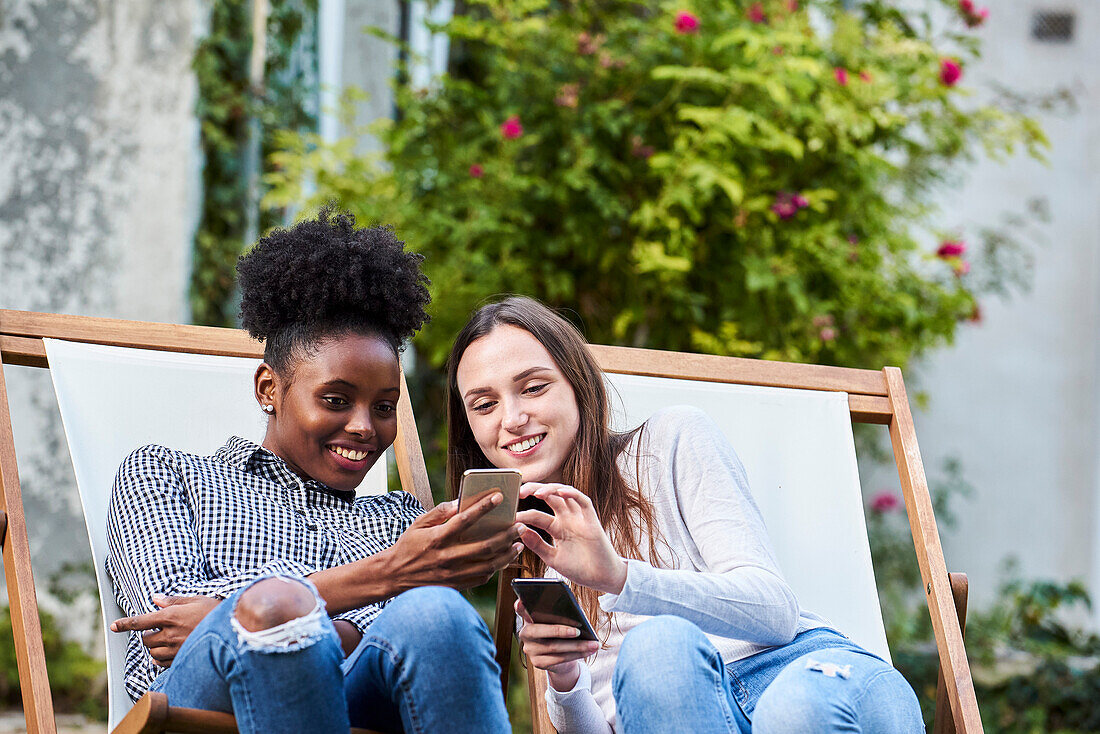 Smiling young friends using smartphones in park