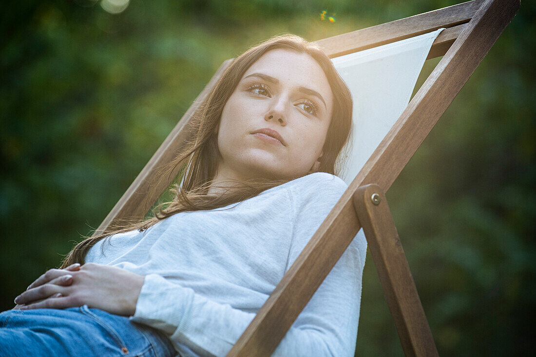 Thoughtful young woman with hands on stomach leaning on chair