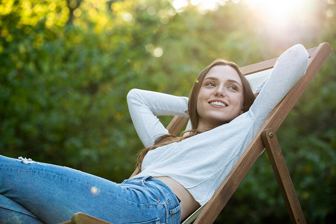 Smiling young woman with hands behind head leaning on chair