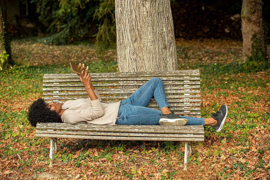 Young woman using digital tablet while lying on bench in park