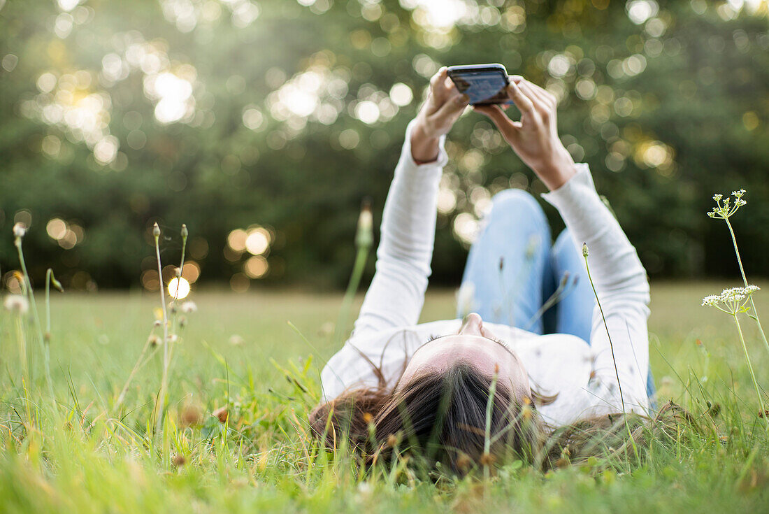 Young woman using smart phone while lying in park, Orgeval