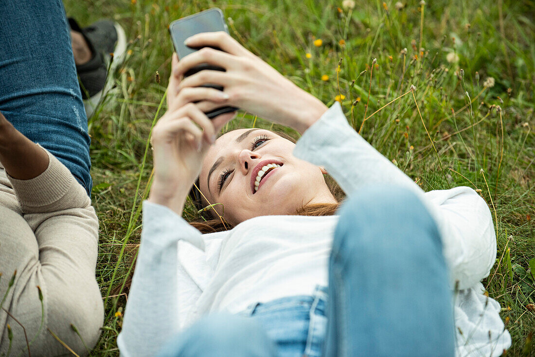 Junge Freundinnen liegen im Gras und benutzen ihr Smartphone im Park