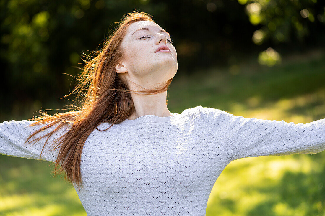 Young woman with eyes closed stretching her arms in park